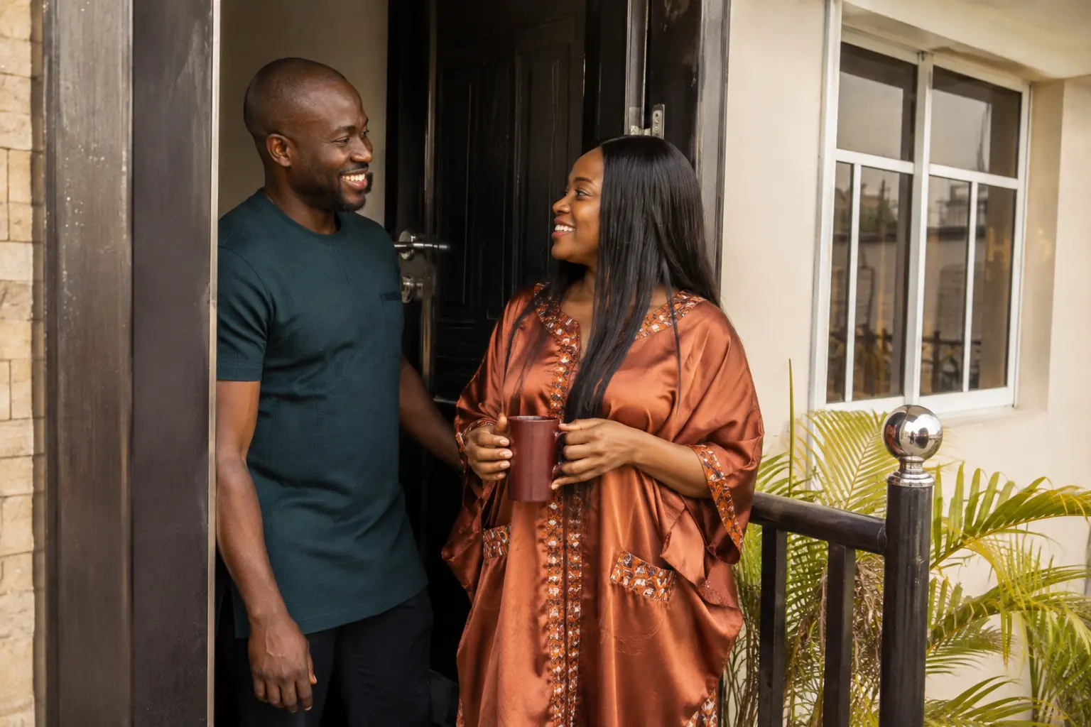 A couple standing in the doorway of their home, smiling at each other over a morning cup of tea.